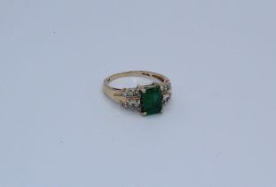 An emerald and diamond set dress ring featuring a central emerald cut stone, approximately  8mm x