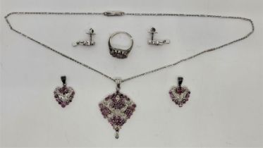 A white metal, ruby and diamond pendant, ring and drop earrings en suite, the pierced pendant