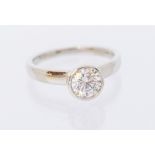 A diamond and platinum solitaire ring, comprising a rub over set round brilliant cut diamond,