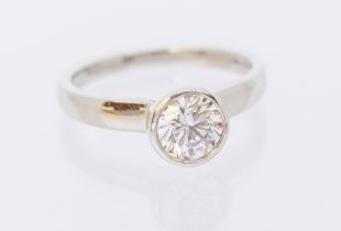 A diamond and platinum solitaire ring, comprising a rub over set round brilliant cut diamond,