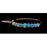 An opal and 18ct gold hinged bangle, comprising nine graduated round cabochon opals, with blue and