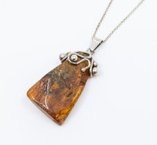 An amber and silver modernist style pendant and chain, comprising a rough cut amber with ornate