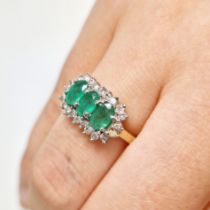 An emerald and diamond 9ct gold ring. Three emerald type stones surrounded by small diamonds set