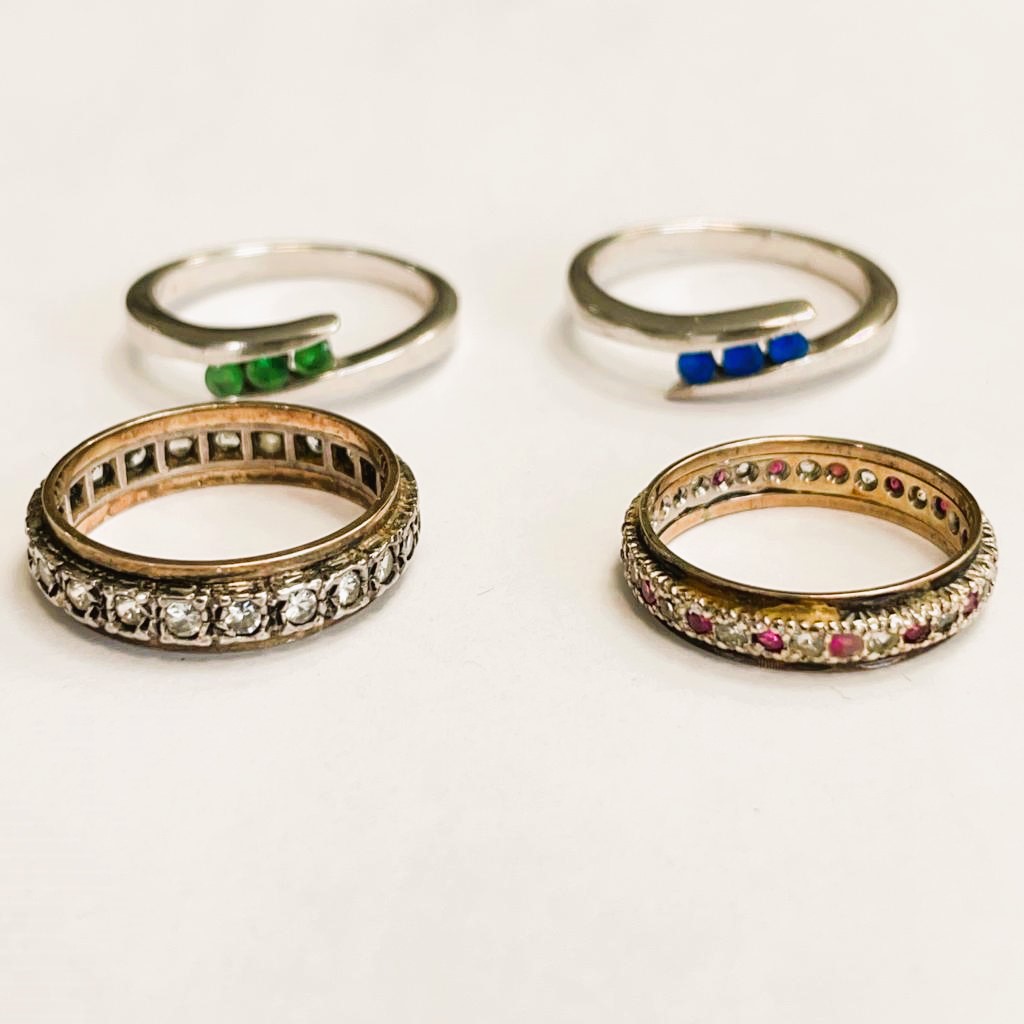 Four rings to include: Two silver metal rings (one set with 3 emeralds, one set with sapphire