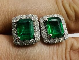 A pair of emerald and diamond earrings. Featuring two emerald cut Emeralds, each surrounded by 16
