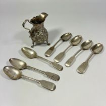 A silver embossed cream jug London 1830-36 S.M and 7 silver table spoons, total approx 250grams.