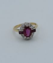 A ruby and diamond ring, the principal oval cut stone with baguette shoulders, claw mounted within a