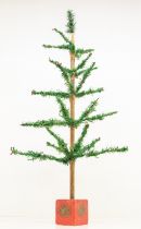 A 1920s Christmas tree, mounted on a red-painted wooden stand with a simple decorative emblem,