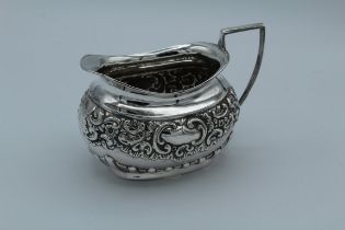 An Edwardian silver cream jug with floral repousse decoration around a vacant cartouche, angular