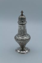 A Victorian silver sugar caster of bellied form, with urn finial, lappet and floral repousse