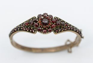 A Victorian Bohemian garnet metal hinged bangle, comprising a central flower motif set with rose cut