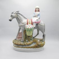 A large Staffordshire figure of a girl astride a donkey with a large basket of fruit Date: Circa