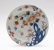 A 18th century style Delft ware charger, decorative with a design in blue, red, yellow and green.