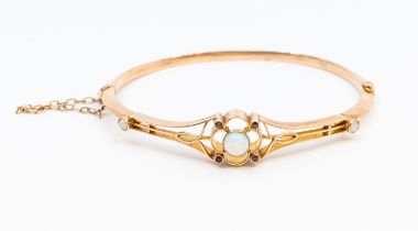 An Edwardian opal and ruby set 9ct rose gold hinged bangle, comprising an open work quatrefoil motif