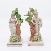 A pair of Staffordshire figures of a boy and girl standing alongside tree stumps on square bases,