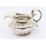 A William IV silver footed cream jug, with gadrooned border and stylised embossed floral design,