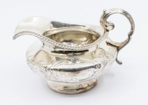 A William IV silver footed cream jug, with gadrooned border and stylised embossed floral design,