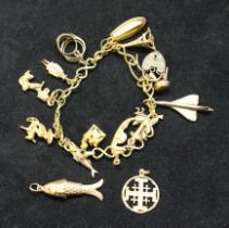 A yellow metal charm bracelet, with a 9ct gold padlock clasp and 13 charms, some of which are