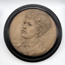 An early 20th Century portrait profile of a young boy, plaster, approx 30cm diam, in ebonised framed