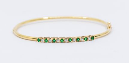 A diamond and emerald 14ct gold hinged bangle, comprising a row of fifteen alternate round mixed cut