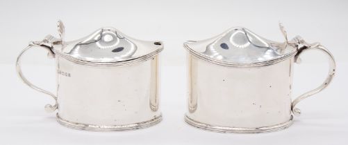 A pair of Georgian style plain silver mustard pot and covers, reeded borders, pierced shell