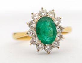An emerald and diamond 18ct gold cluster ring, comprising a central oval mixed cut emerald, approx 6