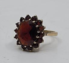 A 9ct. gold and garnet cluster ring, set mixed oval cut garnet to raised centre bordered by fourteen