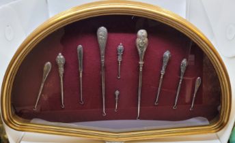 A collection of late 19th/early 20th century button hooks, mounted against burgundy baize in a fan