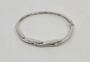 An 18ct. white gold and diamond set hinged bangle, the front fashioned as entwined bands, one set