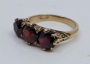 A 9ct. gold and garnet ring, set three mixed round cut garnets above scroll pierced gallery, size UK