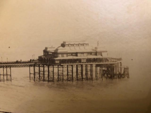 Photograph mounted on card of a seaside resort, pier and beach.