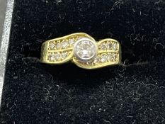 Jewellery: Yellow metal ring seventeen stone crossover, centre rub over set with a single