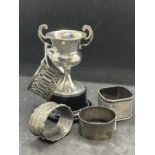 Hallmarked Silver: Four assorted napkin rings and a small two handled trophy on a fitted plastic