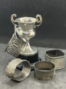 Hallmarked Silver: Four assorted napkin rings and a small two handled trophy on a fitted plastic