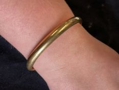 Jewellery: Yellow metal plain 7mm hinged bangle tests as 18ct gold. Weight 14.3g.