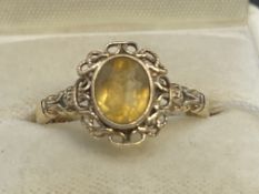 Jewellery: Yellow metal ring set with an oval cut citrine with a rope border and fancy shoulders,