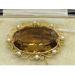 Jewellery: Yellow metal brooch set with an oval citrine with a scroll and pearl surround, tests as