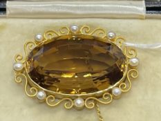 Jewellery: Yellow metal brooch set with an oval citrine with a scroll and pearl surround, tests as