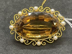 Jewellery: Yellow metal brooch set with an oval citrine with a scroll and pearl surround,