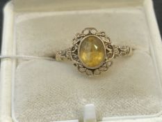 Jewellery: Yellow metal ring set with an oval cut citrine with a rope border and fancy shoulders