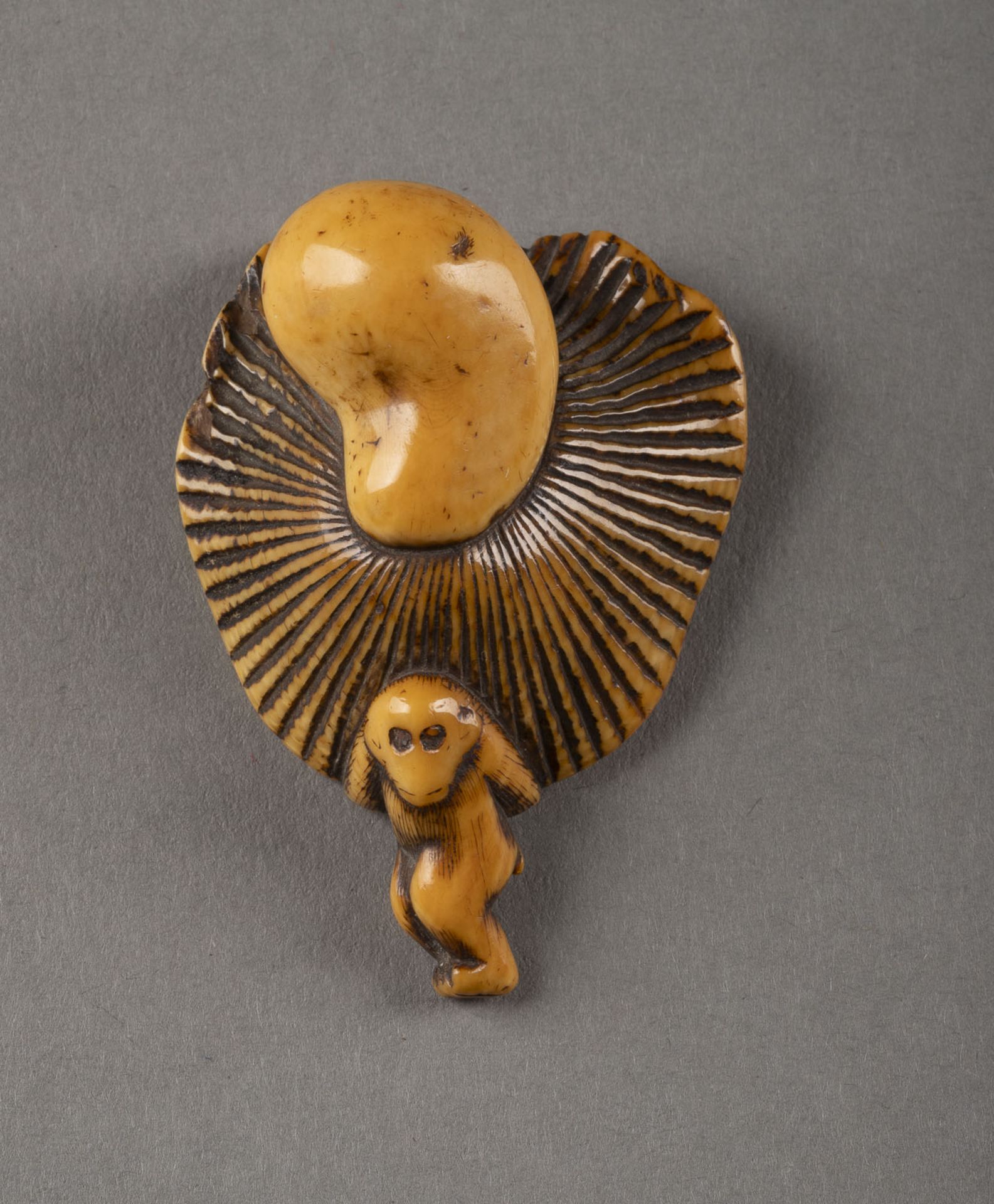 EIN GESCHNITZTES NETSUKE EINES PILZ TRAGENDEN AFFEN AUS ELFENBEIN