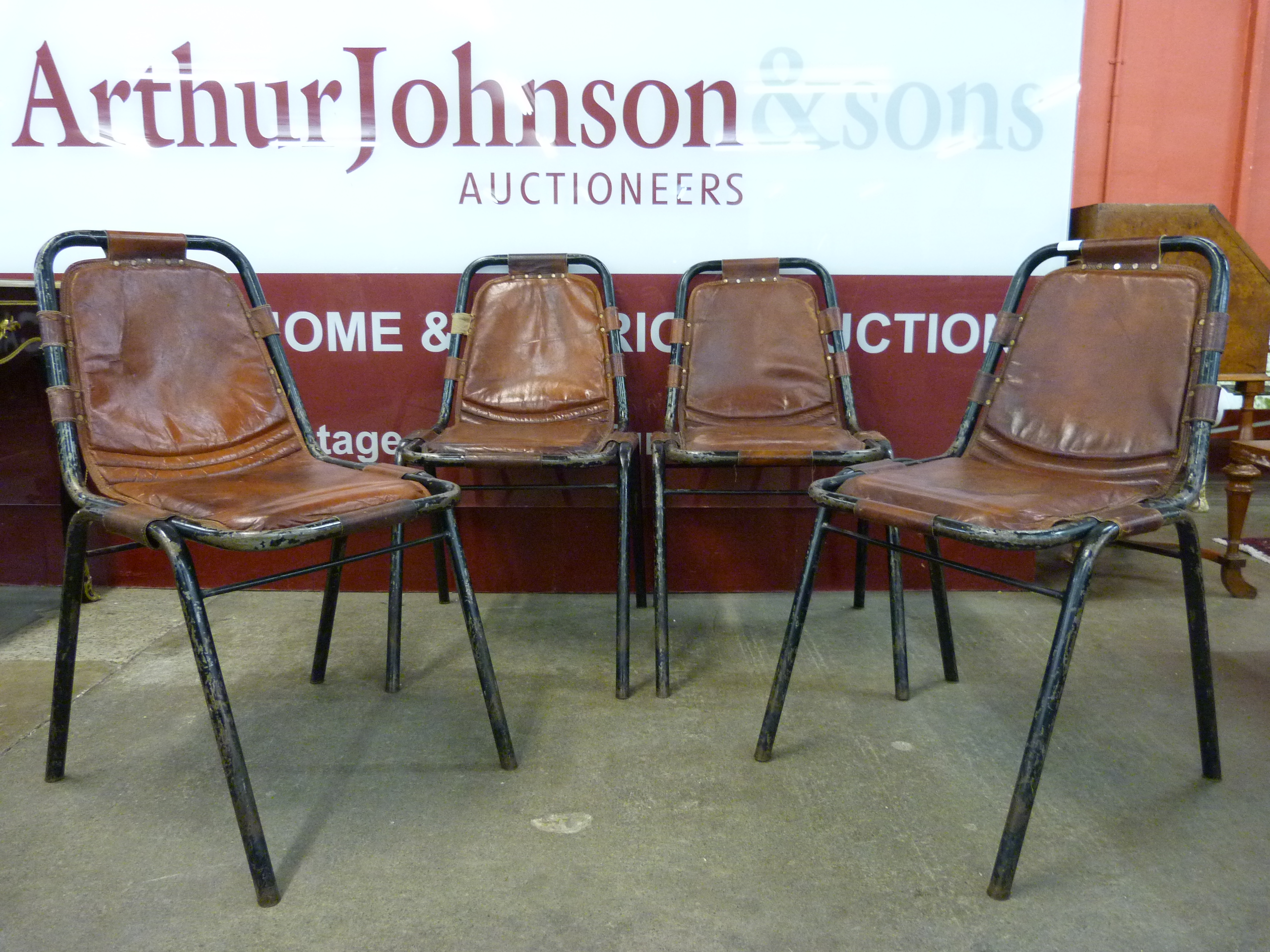 A set of four Les Arcs style black metal and brown leather chairs, attributed to Charlotte Perriand