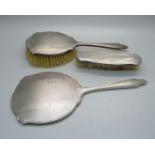 A silver backed Art Deco hand mirror, Birmingham 1944 and two matching brushes, one a/f
