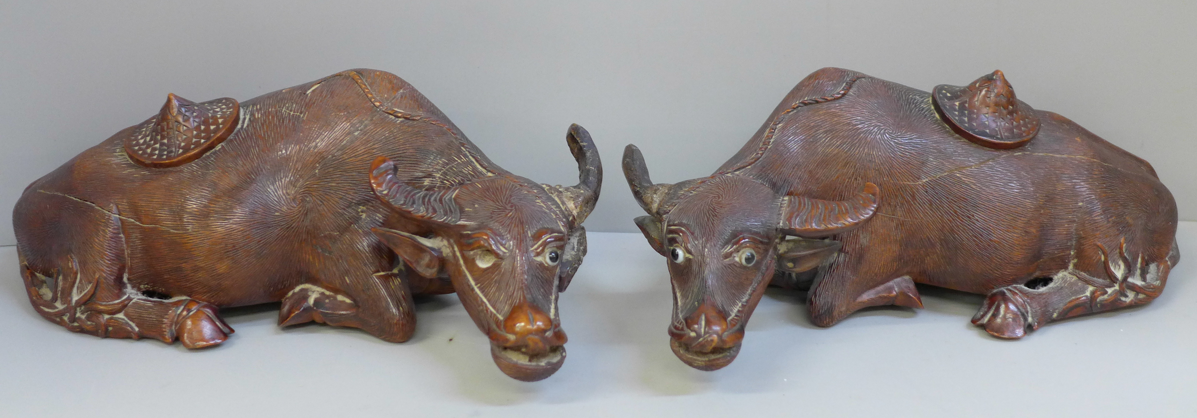 A pair of Chinese carved wooden models of water buffalo, both with damaged horns and splits to body,