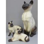 Three Beswick Siamese cats, one large and two medium, largest with chip to ear