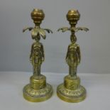 A pair of brass figural candlesticks modelled as a woman taking shade under a palm tree