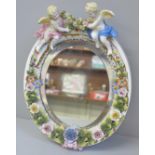 A flower encrusted porcelain mirror decorated with cherubs