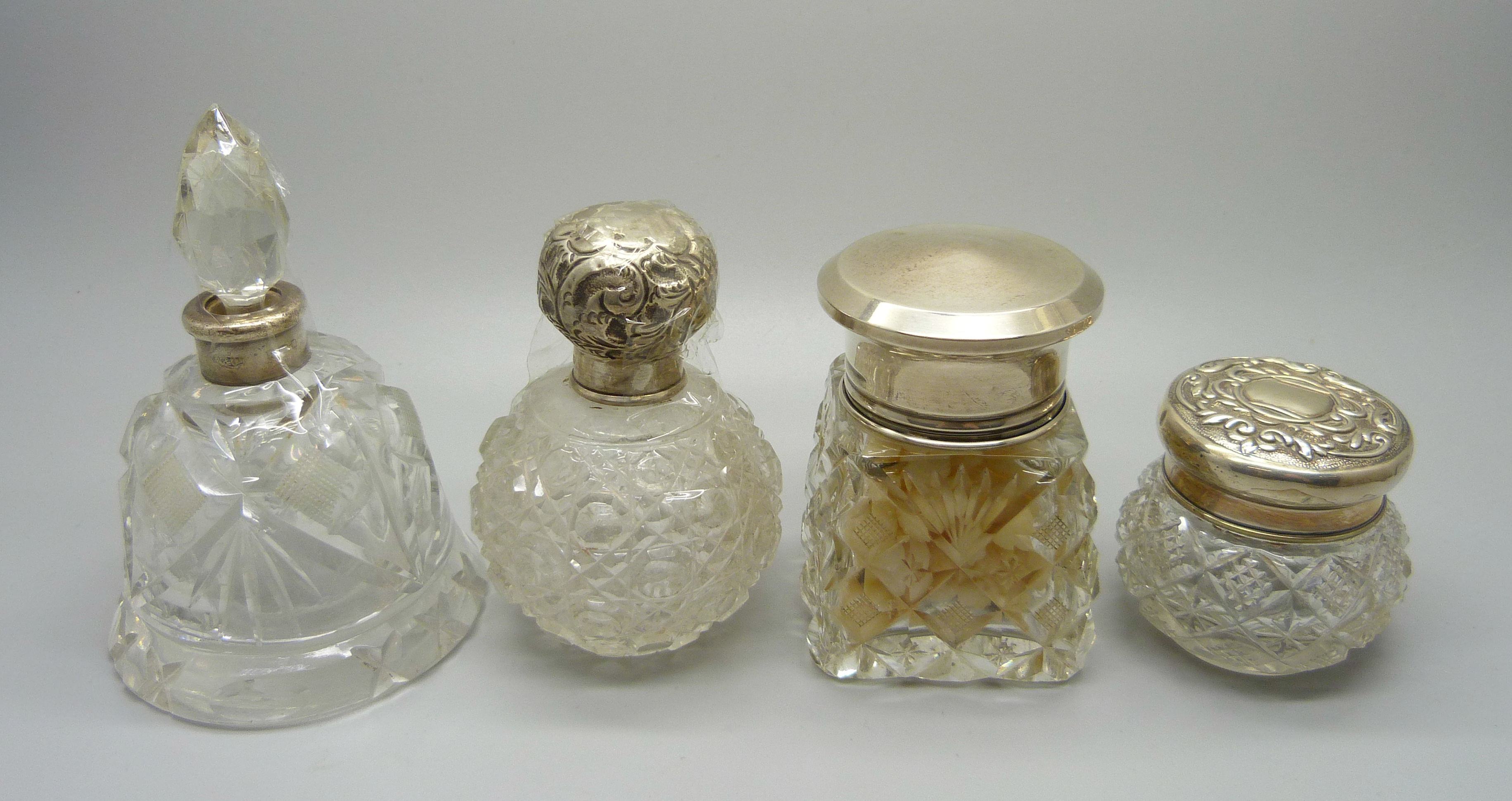 Four silver topped glass scent bottles/dressing table pots, including a scent bottle in the shape of