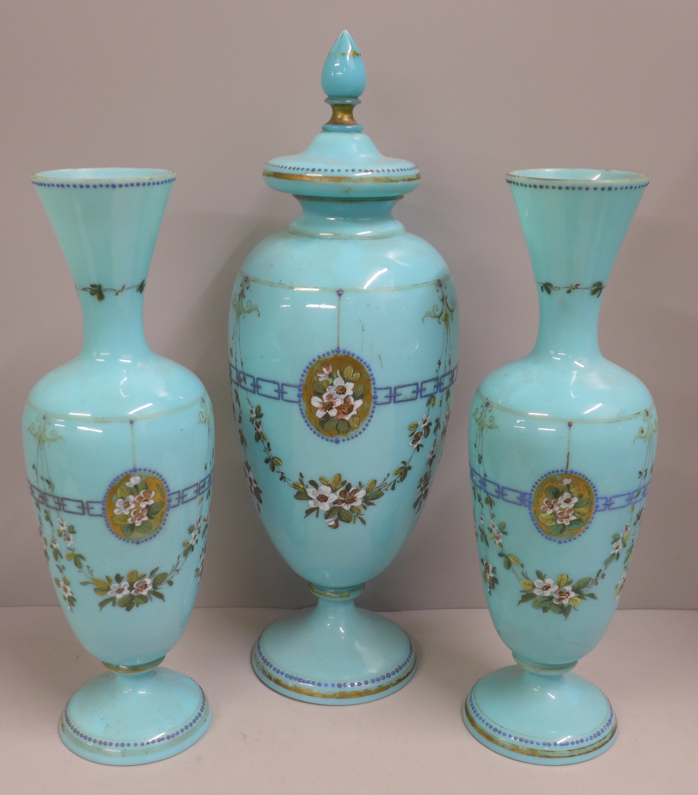 A pair of blue opaline glass vases and one taller lidded vase, enamel painted of swags of flowers