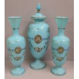 A pair of blue opaline glass vases and one taller lidded vase, enamel painted of swags of flowers